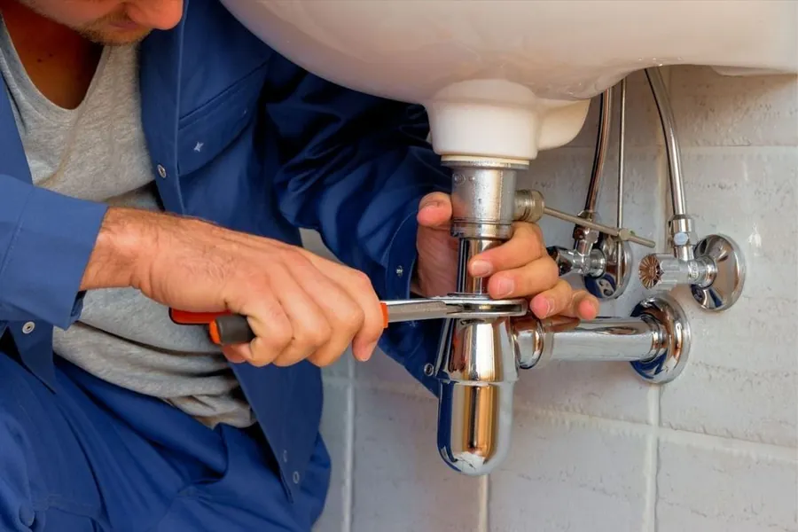 Plumber in blue overalls repairing a sink trap with a wrench