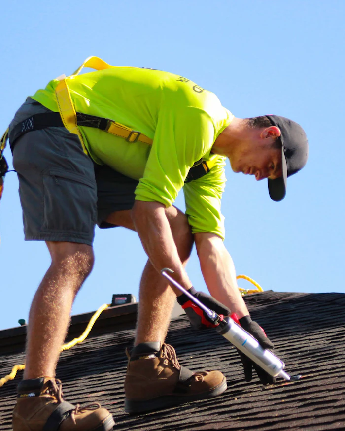 A roofer in a safety harness working on a shingled roof.